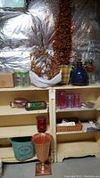 Shelf of various home decor and craft items, including jars, planter urn, wicker basket, and cups