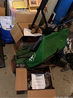Italian Brill push mower with green fabric grass catcher bag, viewed from the side with boxes and basement surroundings visible