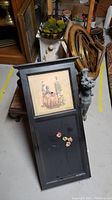 Black wooden magnetic board with framed art and flower magnets resting against a plastic gargoyle and wood frames in background.