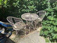 Full set of round metal outdoor table with two chairs under leafy shade, showing the overall design and condition.