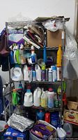 Front view of metal utility shelf fully loaded with various cleaning supplies and household items, showing overall condition and usage.