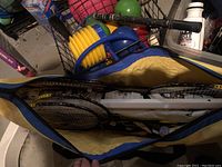 Yellow and blue Sportcraft branded backpack partially open showing badminton and tennis rackets and other sporting equipment inside
