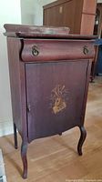 Front and side view of the vintage wood cabinet with a musical design on the front door.