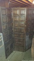 Full view of the tri-fold wooden room divider in a basement setting, showing the raised panel design and metal hinges.