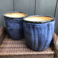 Two blue glazed ceramic pots displayed on woven outdoor furniture, showing exterior sides.