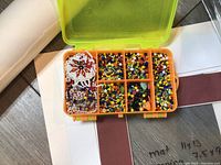 Photo showing open two-sided bead container with assorted beads in multiple compartments and bead designs.