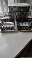 Two black metal wire baskets with brown woven pattern stacked side by side on a white table, with their packaging box behind them