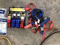 Ratchet straps in red and blue colors with metal ratchets and hooks displayed on the ground.