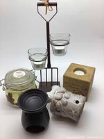 Photo showing rustic metal stand with glass tea light holders, ceramic wax burners, decorative candle in jar, and square candle holder