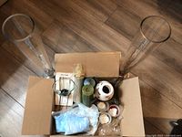 Top view showing two tall clear glass vases flanking a cardboard box containing various candle holders, candles, and candle-making supplies.