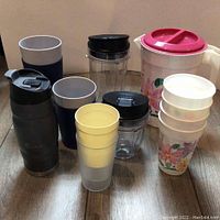 Various drinkware items including Ninja Nutri cups, Bubba water bottle, plastic pitcher and cups, arranged on the floor