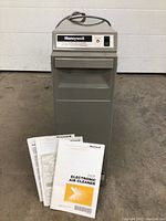 Front view of the Honeywell F50F electronic air cleaner standing upright showing control panel and manuals on the floor in front.