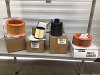 Photo of all five miscellaneous generator air filters displayed on metal shelf, showing different sizes and shapes mostly cylindrical with pleated paper media