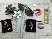 Photo of assorted hair accessories and costume jewelry including hair clips, eyeglasses, rings, charm bracelets, and necklaces on a table