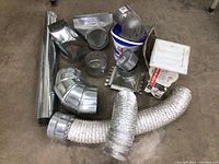 Overall photo showing all miscellaneous ductwork components including pipes, elbows, flexible ducts, and vent covers spread on a concrete floor.