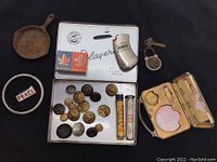 Various vintage items arranged showing buttons, lock with key, metal compact, and small pill bottles.