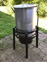 Full view of the aluminum deep fryer pot on the black metal stand, showing the lid and handles.
