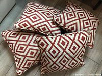 Four outdoor square pillows arranged flat on a wood floor showing the diamond pattern and piped edges.