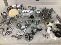 Overview of assorted plumbing service parts including chrome faucet handles, pipes, fittings, washers and valve stems spread out on a flat surface.