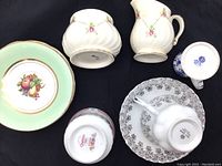 Porcelain items including cream pitcher, candle holder, two bowls, and teacup with saucer, displayed on black background.
