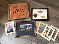 Group photo of five framed prints and empty frames on wooden floor