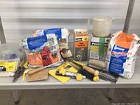 Photo of miscellaneous tiling and drywall tools and grout bags arranged on a table.