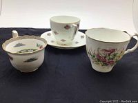 Photo showing three vintage floral ceramic cups and one matching saucer arranged on a black cloth background.