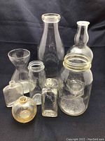 Full view of the collection showing various shapes and sizes of clear vintage glass bottles and containers arranged on dark fabric background.