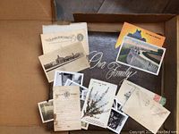 Vintage postcards and black and white photos displayed inside a cardboard box.