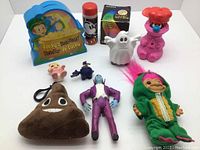 Photo showing an assortment of vintage toys including a Lucky's Pot of Gold plastic sign, pink poodle, ghost figurine, small dolls, helicopter, plush poop emoji, vampire figurine, cartoon tube, and a troll doll in green dinosaur costume.