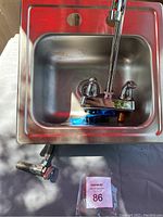 Stainless steel sink basin with faucet placed inside, shows entire sink with faucet and attachment outdoors.