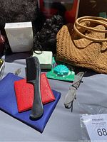 Photo showing wigs, sealed Guerlain perfume box, comb, wallets, glasses and woven handbag