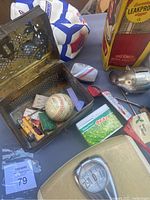 Photo of perforated metal box containing various small items including a used baseball, adjacent vintage Thermos product and a portion of a Fisher-Price Peas box