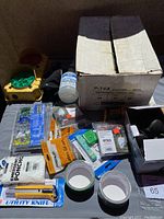 Photo of various small hardware and safety items including emergency poncho, utility knife, duct tape, screws, and safety light.