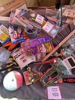 Photo of mixed household items and emergency supplies spread out, showing metallic stapler, brass bell, emergency ponchos, and adhesive tapes.