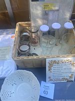 Box containing Paris Musee embossed glass jar, three vintage milk bottles with lids, several clear glass tumblers, all placed in a wooden crate.
