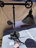 Full view of the black industrial style table lamp showing pulleys, adjustable metal arm, cone shaped shade, and round weighted base.