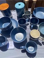 Blue speckled ceramic mugs, bowls, dishes, two canisters with wooden lids, and two wooden spice grinders placed together