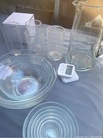 Full view of set including pitcher, 4 drinking glasses, 3 nesting bowls and digital timer on a grey surface.