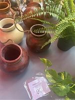 Five pottery pots on rope with reddish-brown and off-white finishes, showing rustic texture and shape.