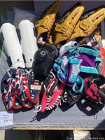 Multiple baseball gloves primarily from Franklin brand in tan leather plus gloves in red, purple, and black, all new with tags. White protective shin guards also included.