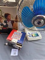 Photo showing the working oscillating fan with blue blades, the boxed knife sharpener, and part of the espresso machine box.