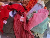 Photo showing assorted women's clothing items including red sweater with candy cane graphics, ribbed sleeveless top with tag, and various colored tops and sweaters.