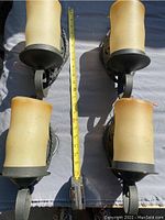 Four black wrought iron wall sconces with melted candle-shaped glass shades arranged on a flat surface with measuring tape showing size around 10 inches tall.