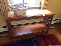 Handmade wooden console table with a basket containing glass figurines and shells placed on top, positioned against a window with curtains.