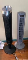 Full view of the two oscillating tower fans side by side; black Honeywell QuietSet and gray Alaba fan.