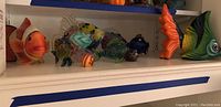 Wide view of the shelf showing a variety of glass fish statuettes in different colors and sizes