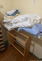 Stack of assorted bath towels, bed sheets, quilts, and pillows resting on a wooden quilt rack.