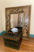 Photo of wall mirror with bird and vine painted frame, Asian-style chest below with mole figurine on top