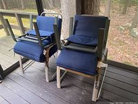 Two outdoor folding lounge chairs stacked upside down, showing metal frame and blue cushions from the back and sides.